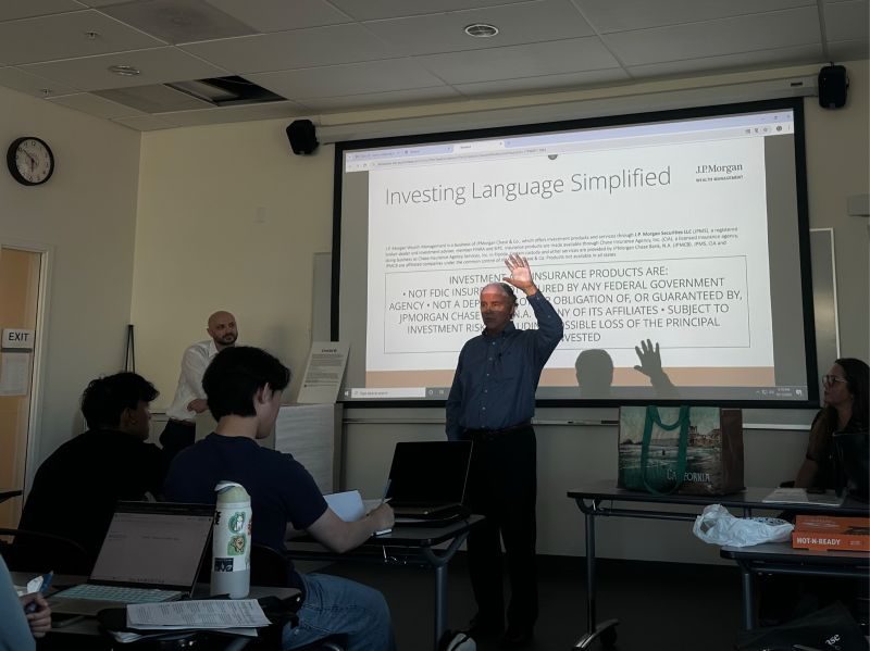 A speaker raises his hand while presenting investing terms