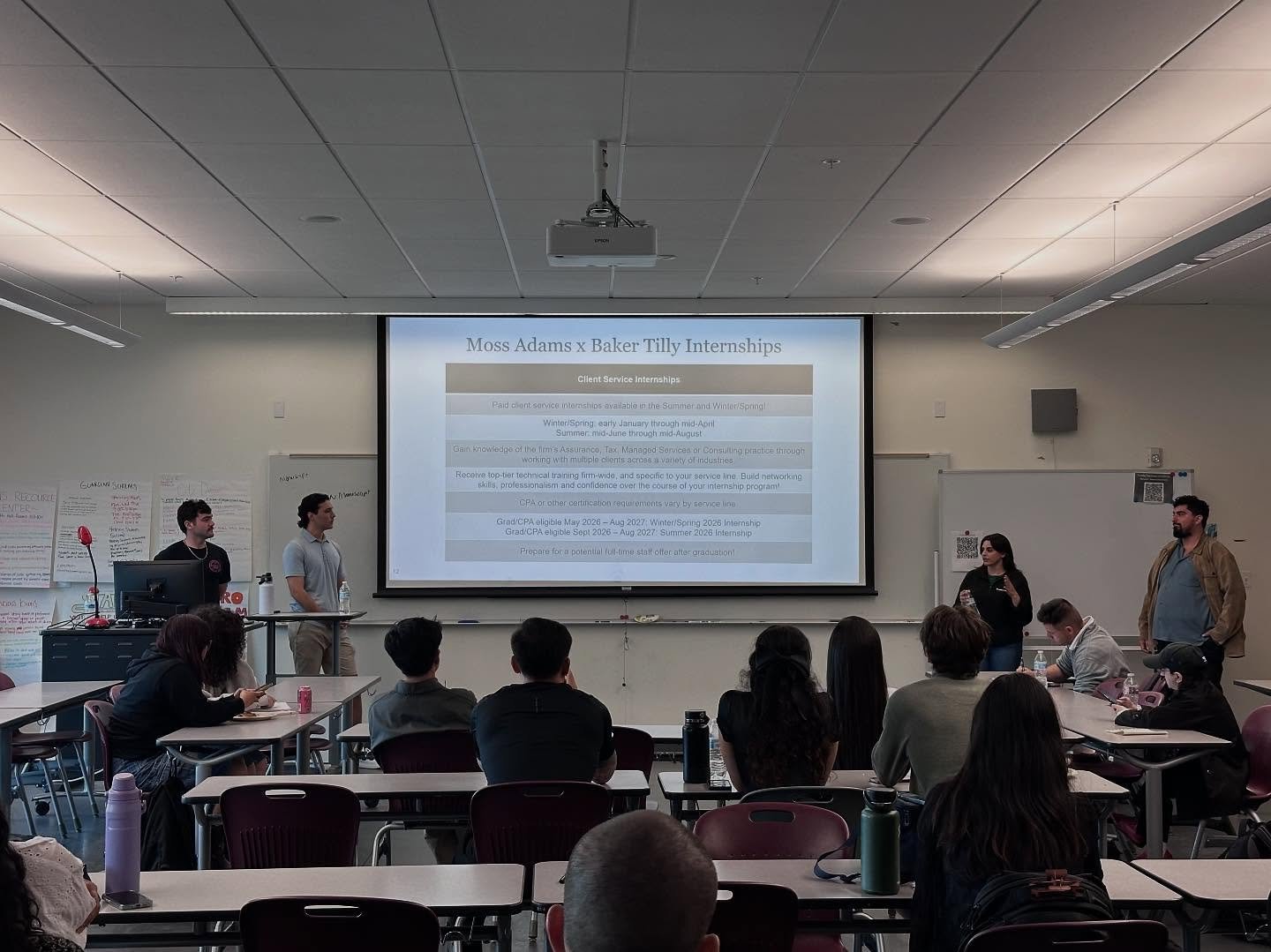Presenters stand beside a slide on Moss Adams x Baker Tilly internships