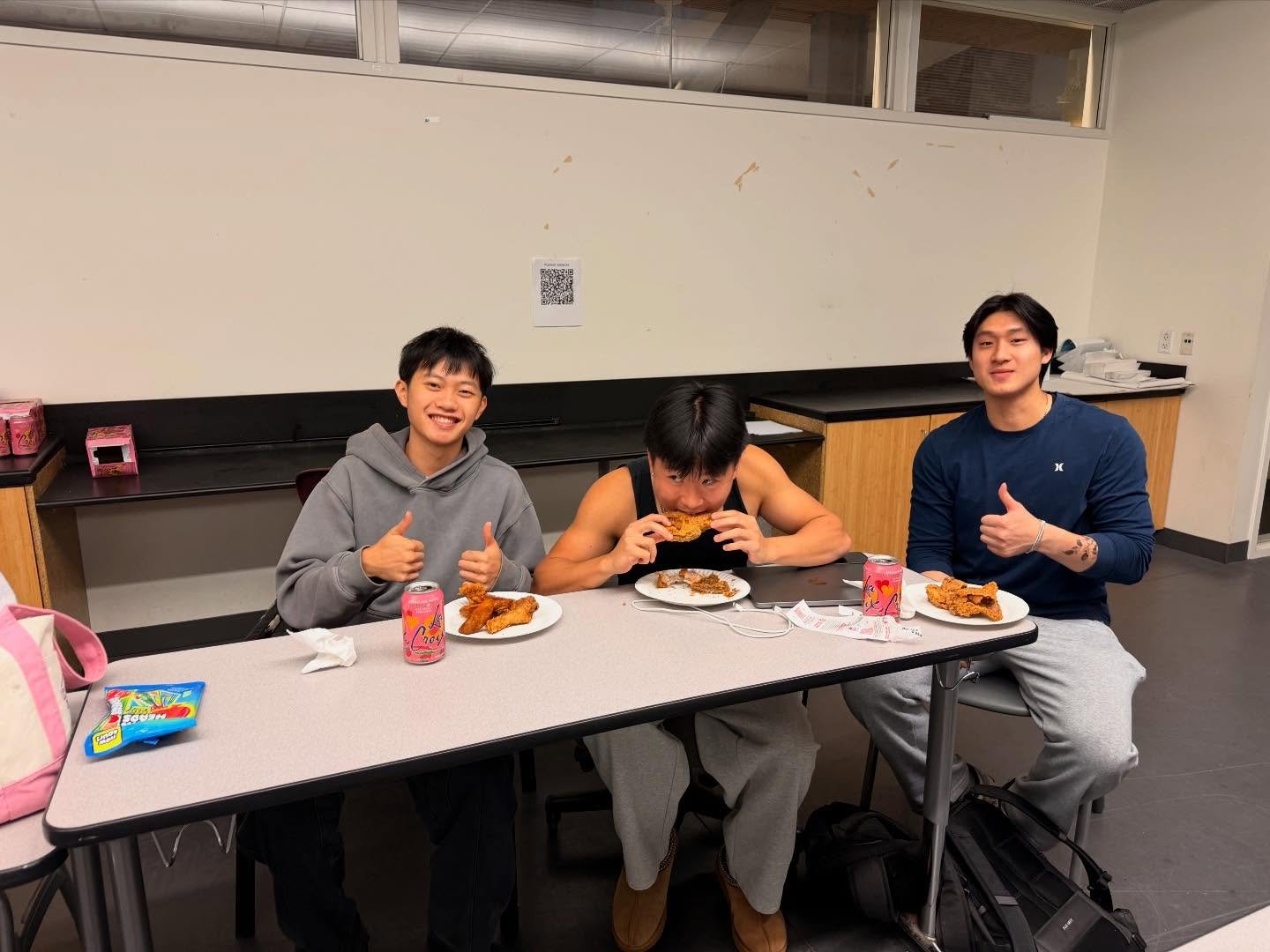 Three members give a thumbs up over plates of food at the meeting